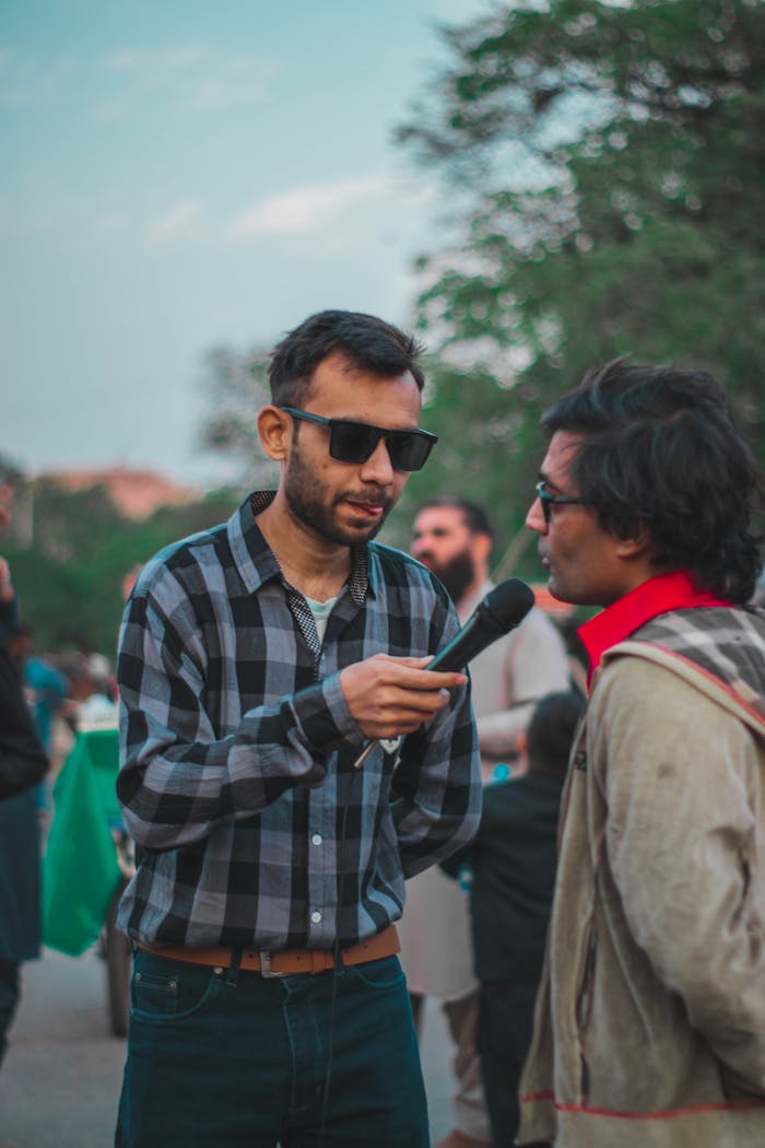 Two men conducting an outdoor interview with a microphone in a casual setting.